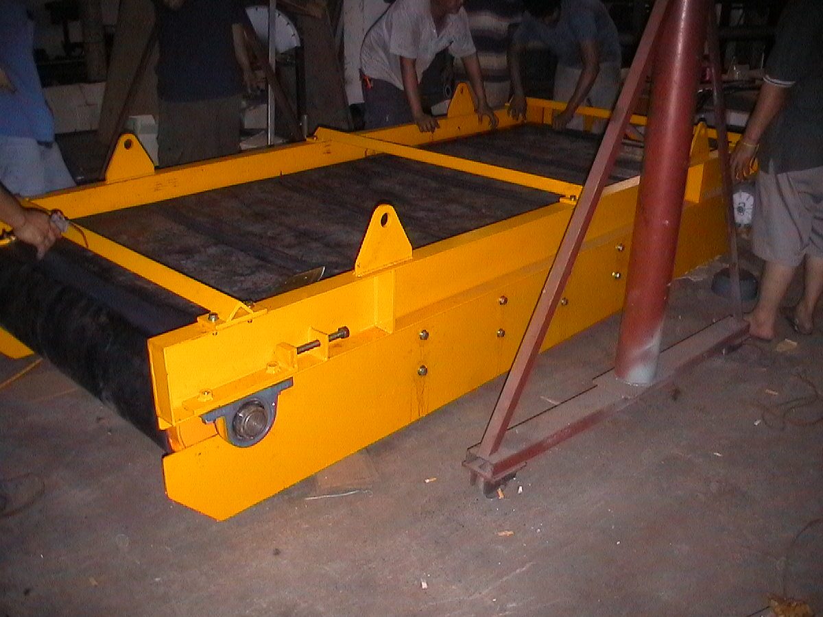 Yellow overband suspension magnet frame with hanging lugs and black ribbed belt on a workshop floor